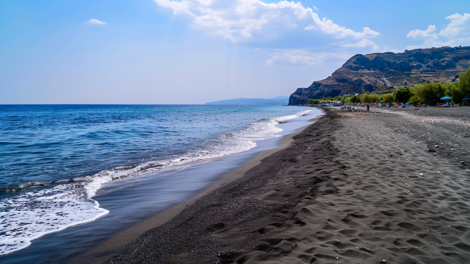 Blue waters crushing against the gray, volcanic sands of a beach in Santorini