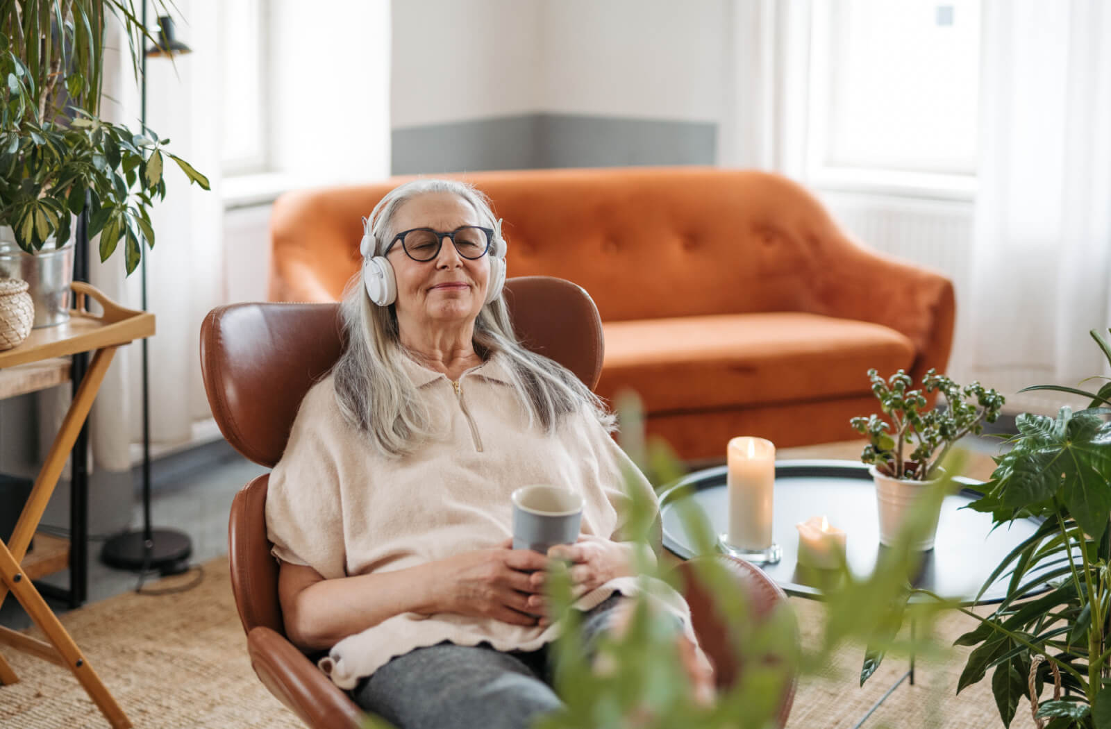 A senior woman listening to music using her wireless headphones while relaxing in a cozy room.