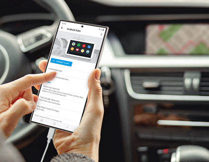 A hand holding a Galaxy S24 Ultra in a car, showing the Android Auto app