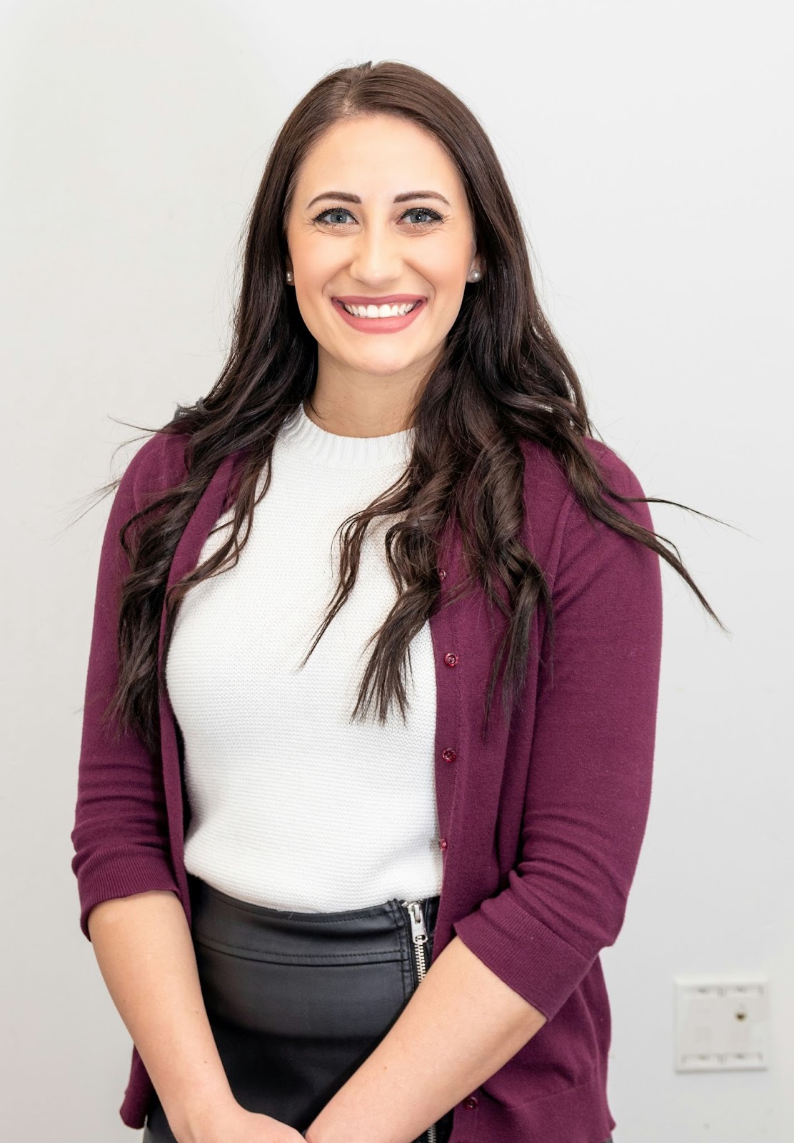 A woman standing in front of a white wall. Neutral colours like white are great background choices for professional headshots.