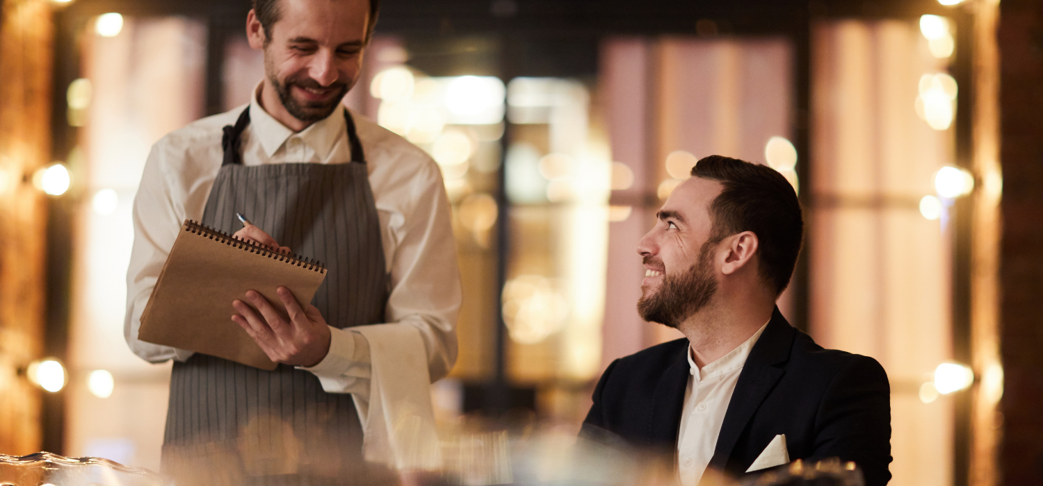 Waiter taking a customer's order in a warmly lit restaurant, exemplifying personalized service as one of Benefits of Omnichannel Marketing for Guest Loyalty