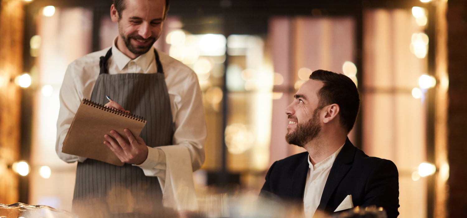 Pelayan mengambil pesanan seorang pelanggan di restoran yang terang benderang, mencerminkan layanan personal dalam omnichannel marketing.