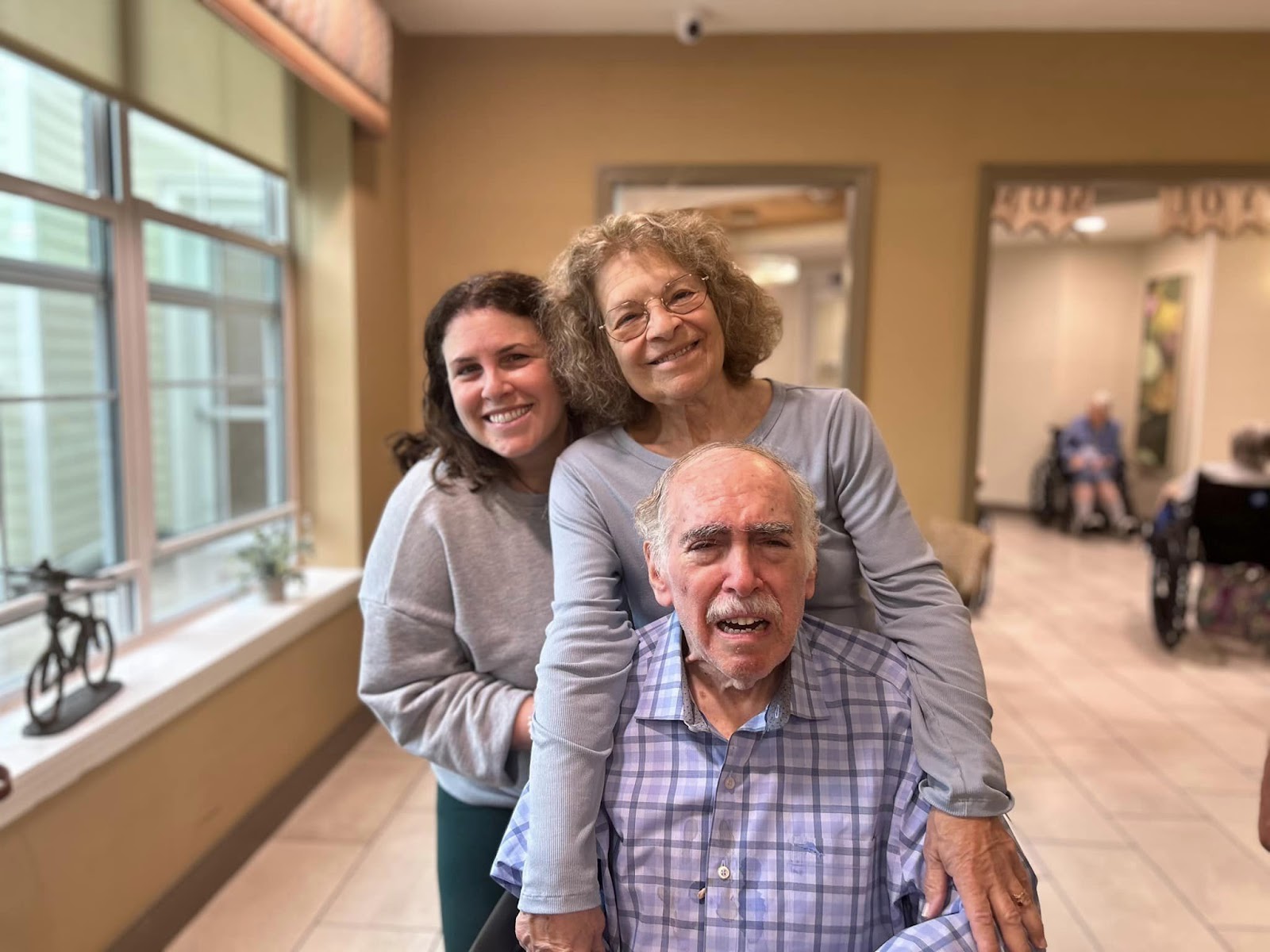 A family smiling with an elderly man sitting in a chair in front of them