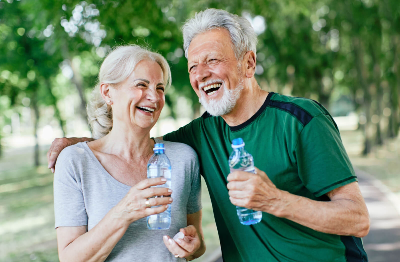 A happy older adult couple in active wear holding an opened bottle of water.