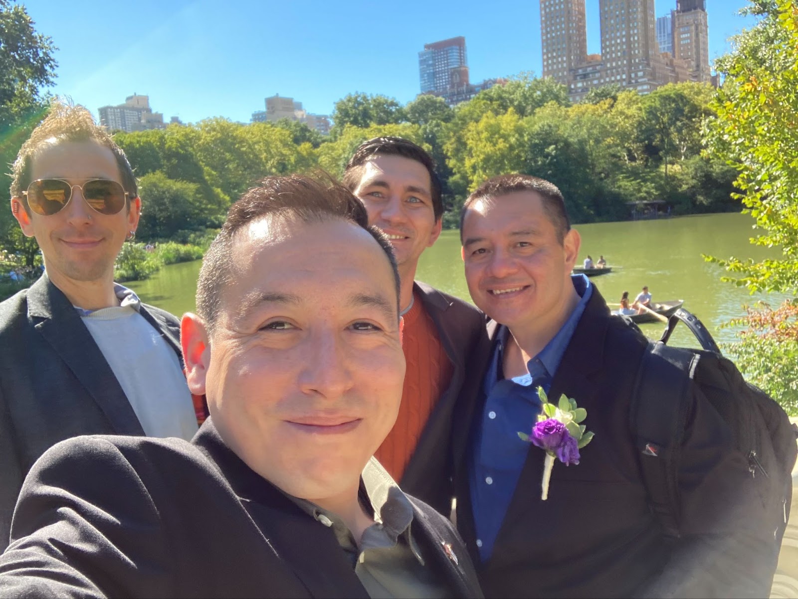 A group of smiling men stand by a lake in Central Park