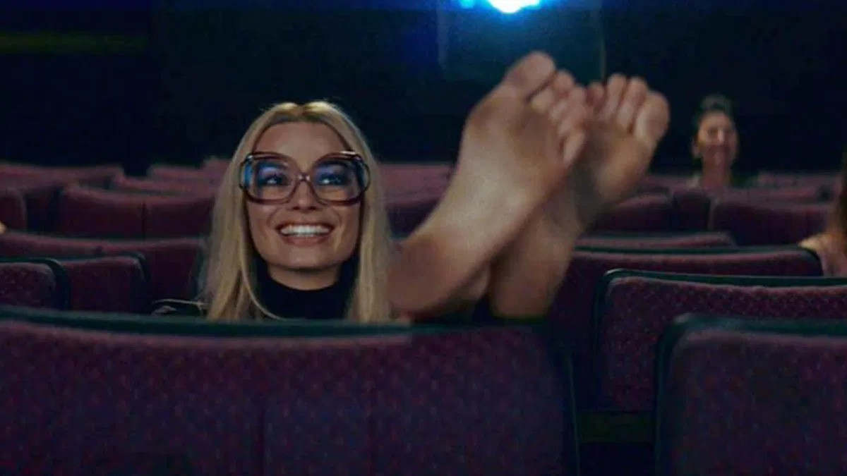 Margot Robbie, interpretando a Sharon Tate en Érase una vez en Hollywood, sentada en una butaca de cine con los pies en alto. 