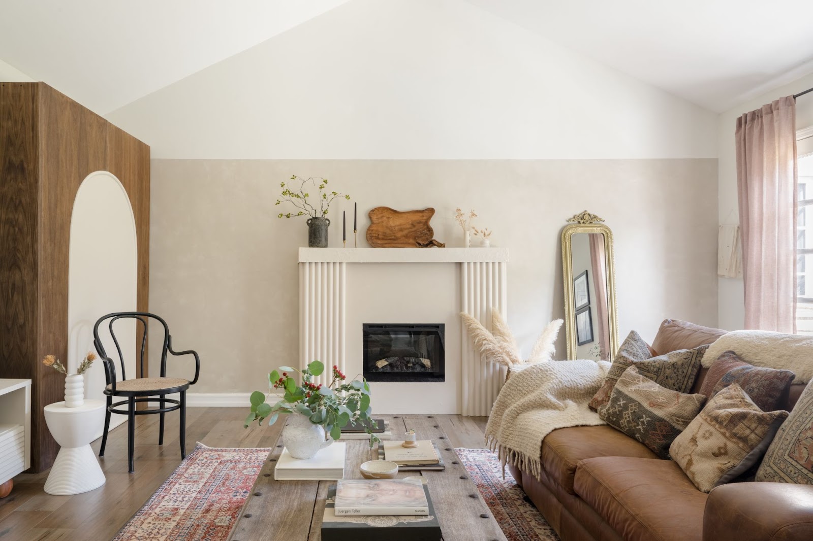 Inviting living room blend: Antique, vintage, and contemporary elements in neutral tones. Warm ambiance with leather sofa, boho pillows, gilded mirror, and a wool rug introducing a touch of red.