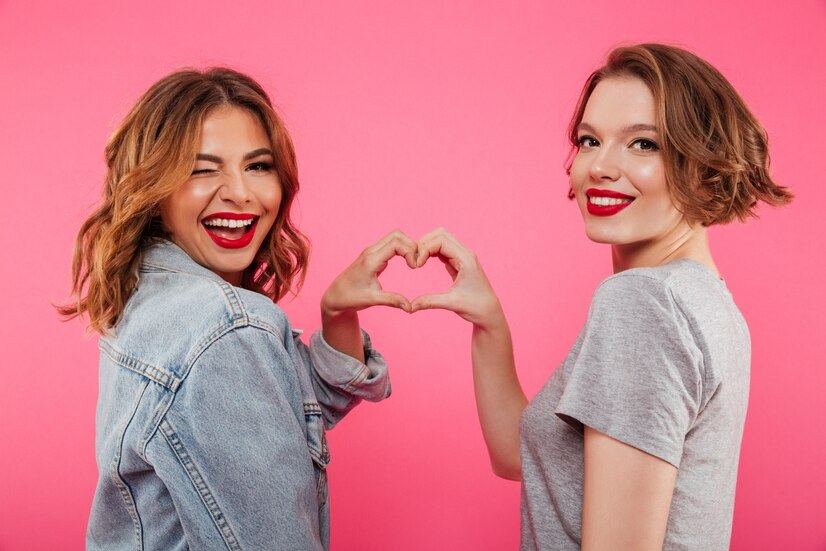 Two girls laughing and forming a heart shape with their hands.