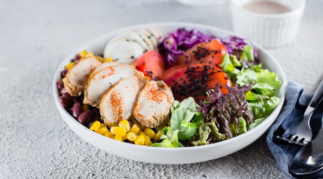 Bowl containing chicken, lettuce, corn, beans, and red cabbage