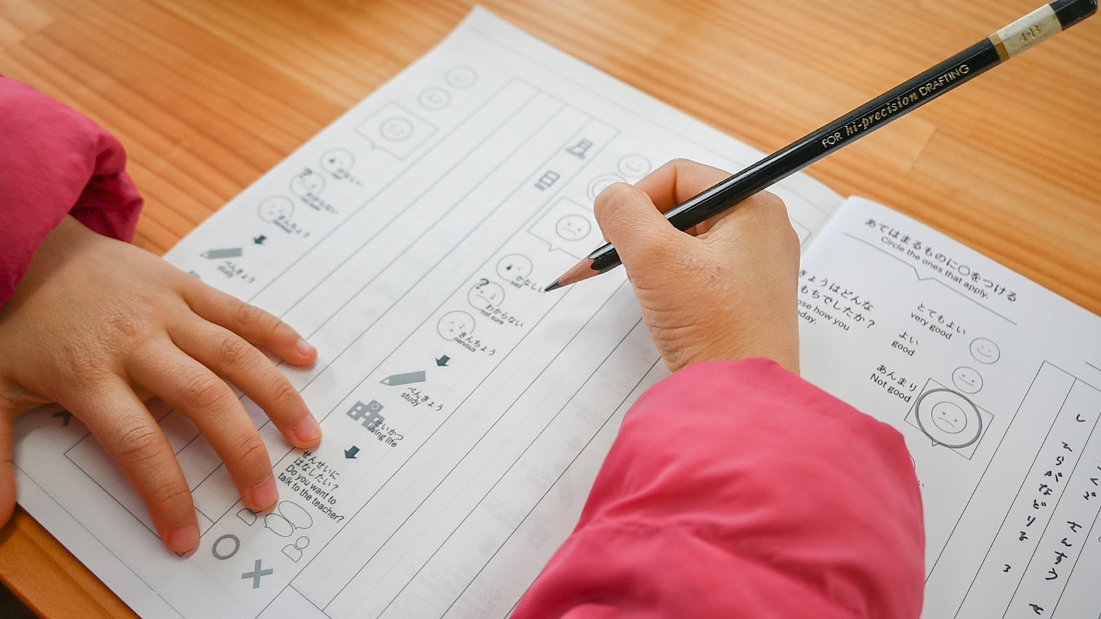 テーブルに広げられた連絡帳に、子供が鉛筆で記入している。