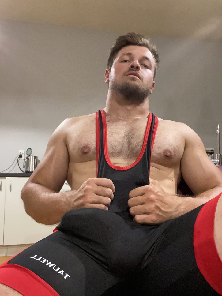 Max Small wearing black and red wrestling singlet showing off his massive penis bulge between the fabric