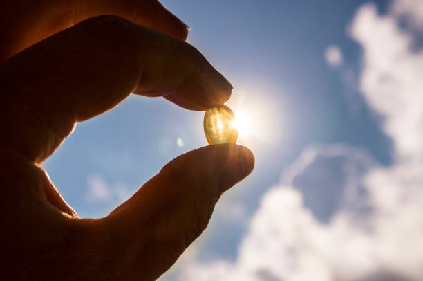 Soft Vitamin D Capsule In Between Thumb and Index Finger Against The Sun