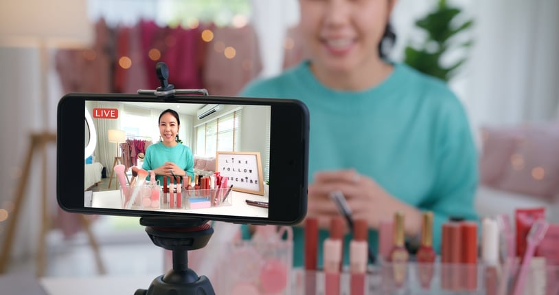 A woman exhibits Influencer Marketing using a phone equipped with a video camera.