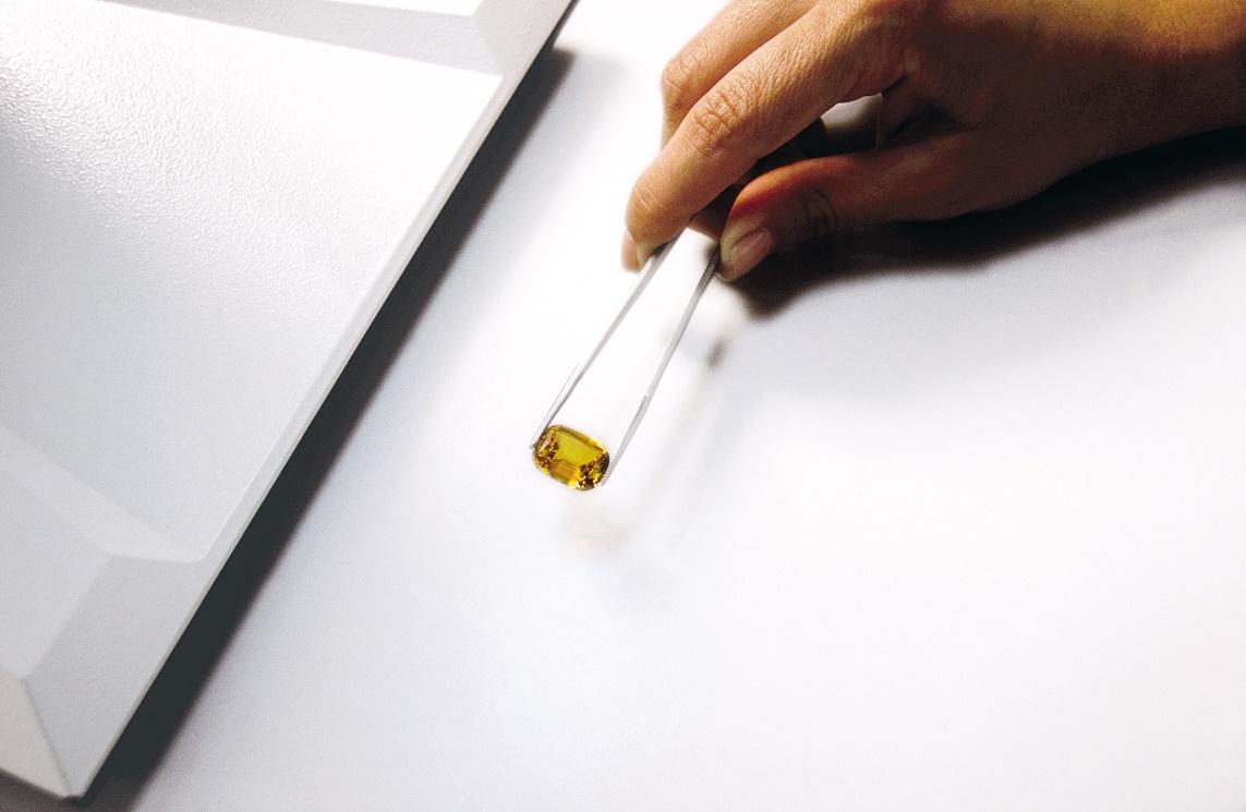 A hand holding a glass tube with a yellow substance

Description automatically generated