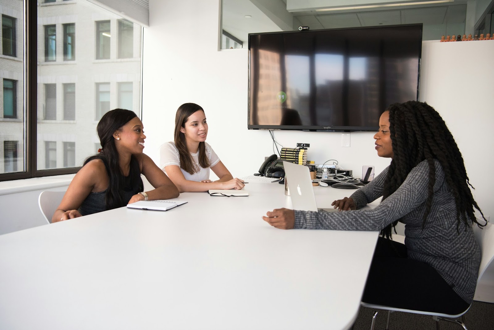 Three women sitting at a table in an office, discussing and working together on a project.