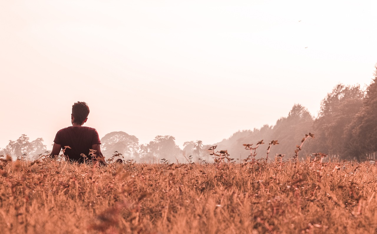  Молодий чоловік сидить на самоті в полі, дивлячись уперед
