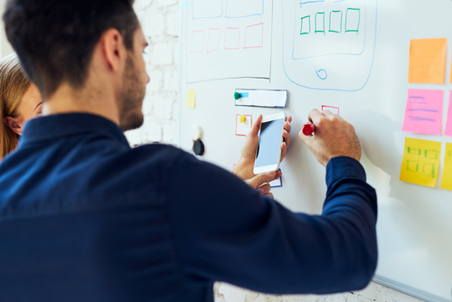 A man and woman collaborate on a whiteboard, enhancing UX by identifying and addressing issues.