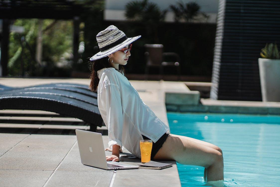 Free Young ethnic woman resting at poolside after distance work on laptop Stock Photo