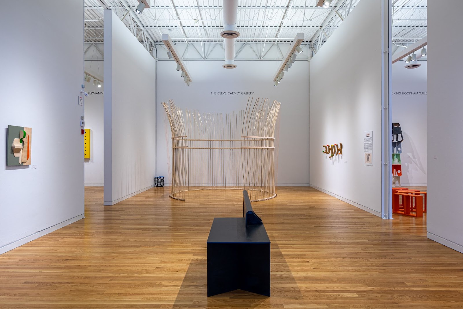 Image: Norman Teagues, Roundhouse, 2024. Poplar, maple, plywood and fishing line. Tall, thin pieces of wood are arranged into a standing structure in the center of a white-walled gallery. Photograph by Siegfried Mueller, courtesy of the Elmhurst Art Museum. 