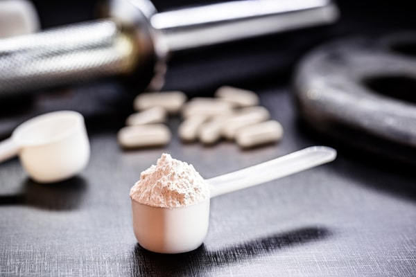 A tablespoon of protein powder with capsules in the background