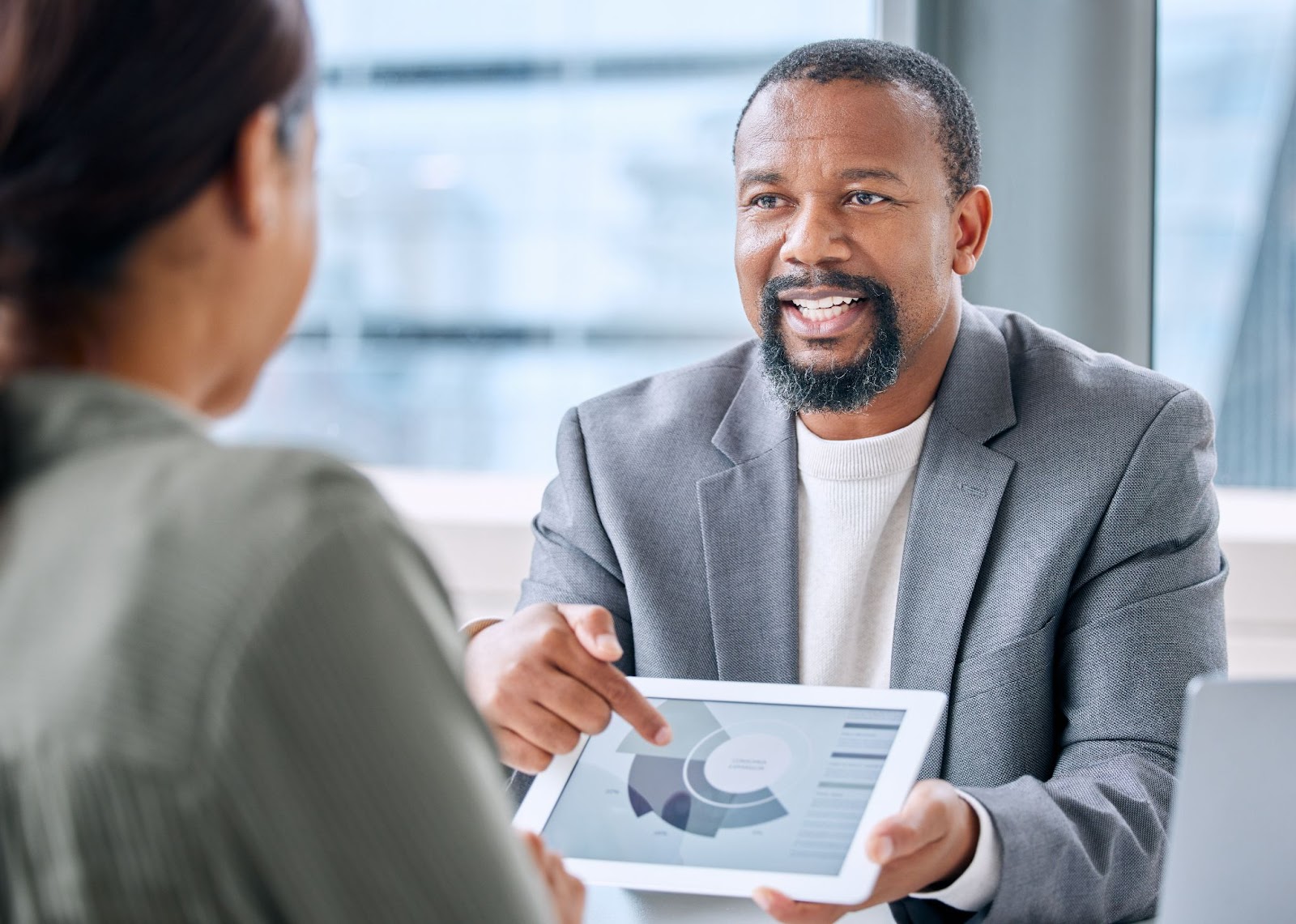 A black male business consultant analyzes a pie chart on his tablet, explaining the data to his female client during a consultation session.