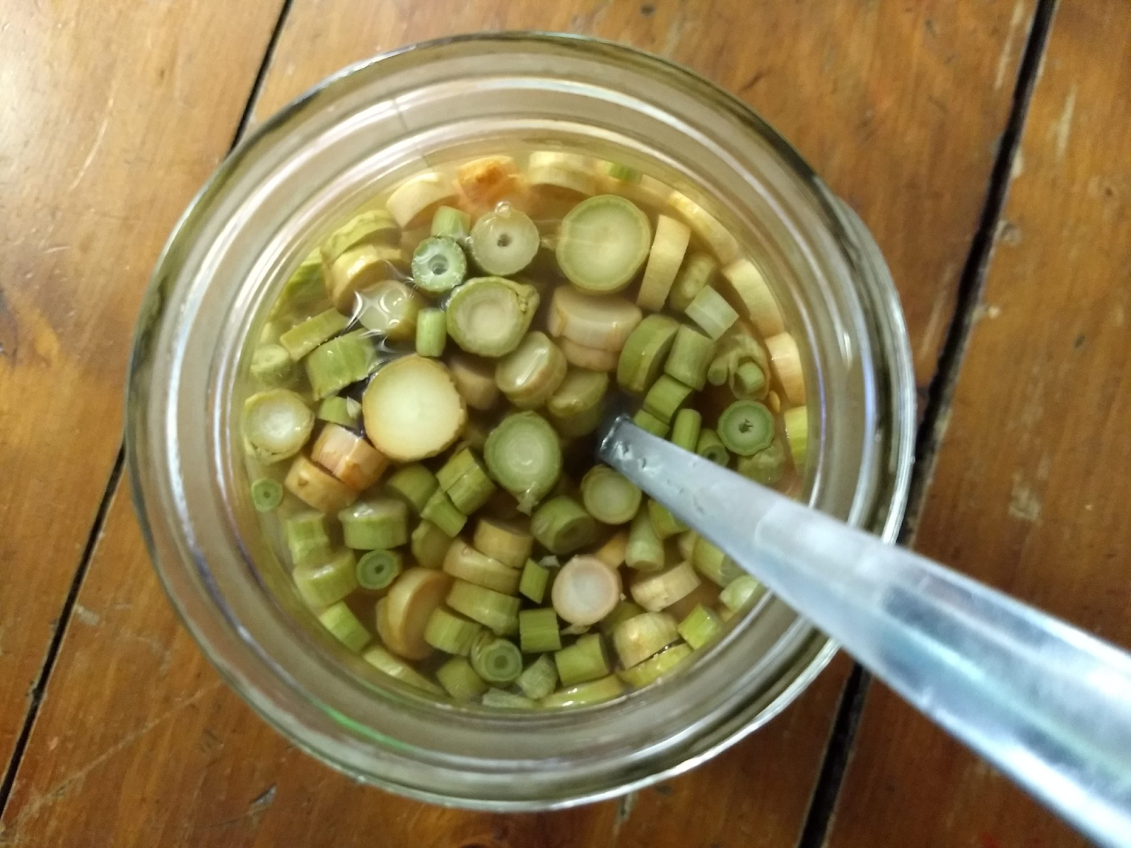 A jar of green onions and a spoon  Description automatically generated