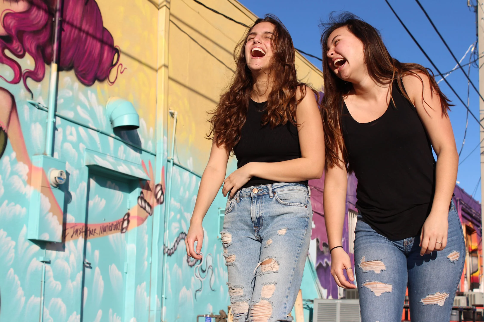 Two women laughing as they walk past a graffiti wall.
