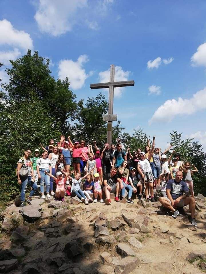 Grupa dzieci stojąca pod krzyżem na szczycie góry.