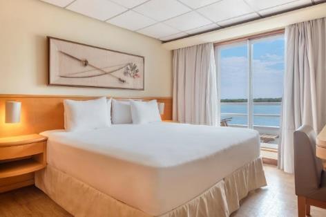 A bed with white sheets and a window with a view of the water

Description automatically generated