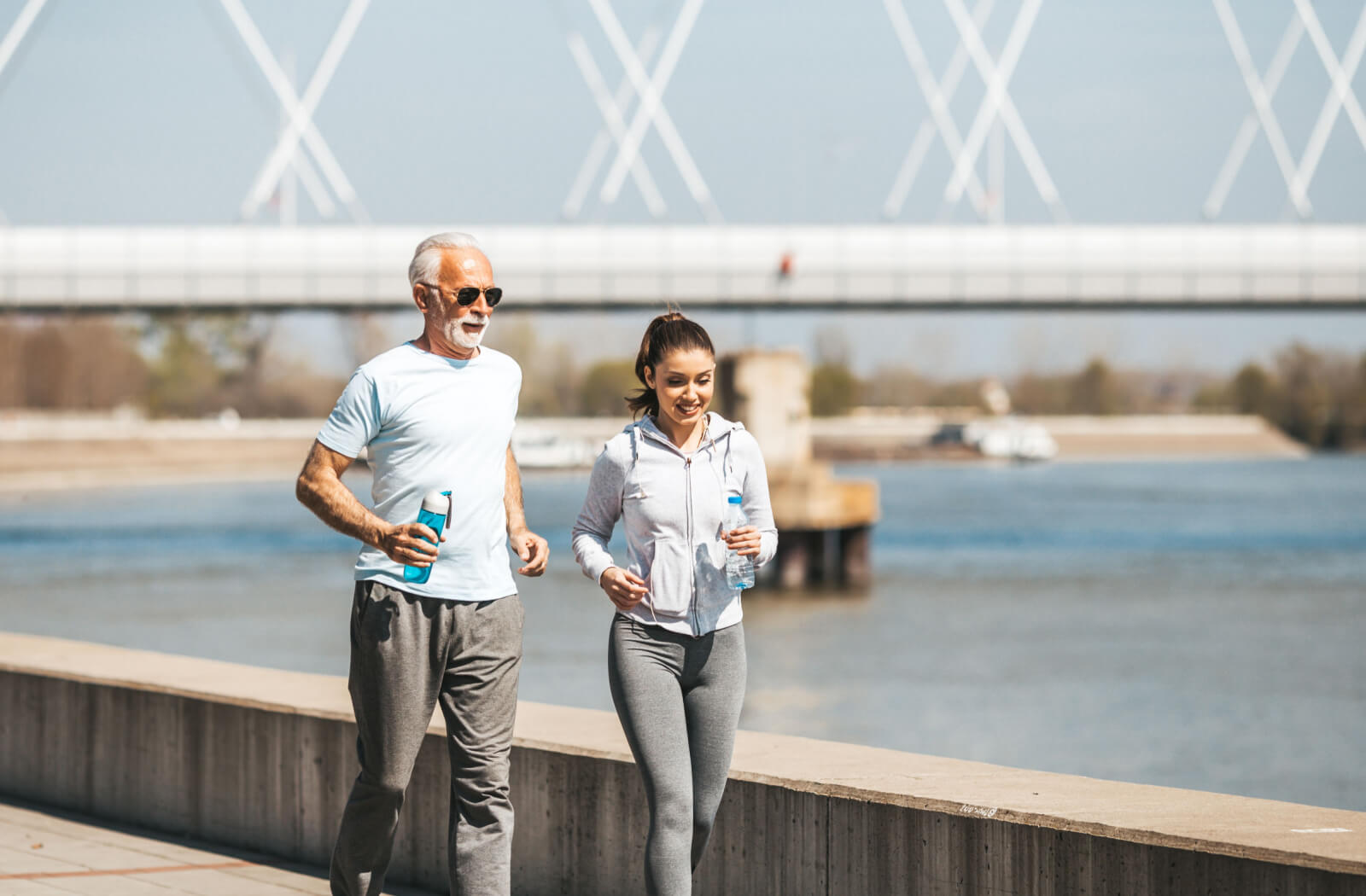 A young woman jogging by a body of water with her older adult father.