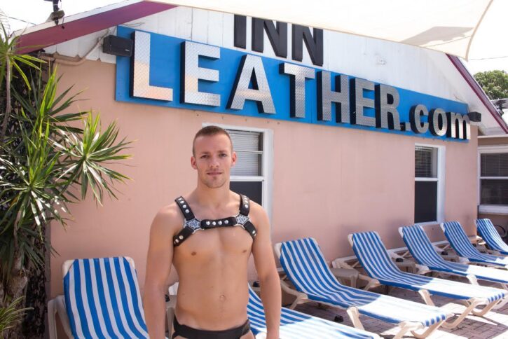gay muscle male wearing studded leather fetish harness shirtless standing in front of innleather.com clothing optional resort building in fort lauderdale florida