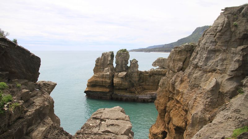 New Zealand national parks - Rocky cliffs and unique stone pillars overlook the blue sea at Paparoa National Park.