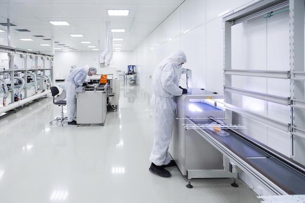 Factory workers in white lab suits and black latex gloves working with some modern equipment in a very clean room