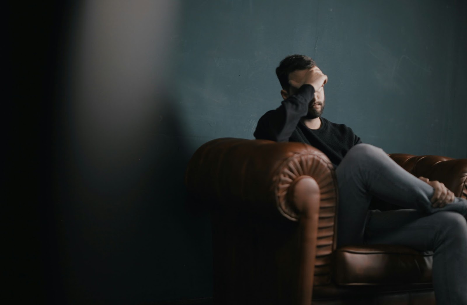 A man holds his head while sitting on a sofa. He look stressed.