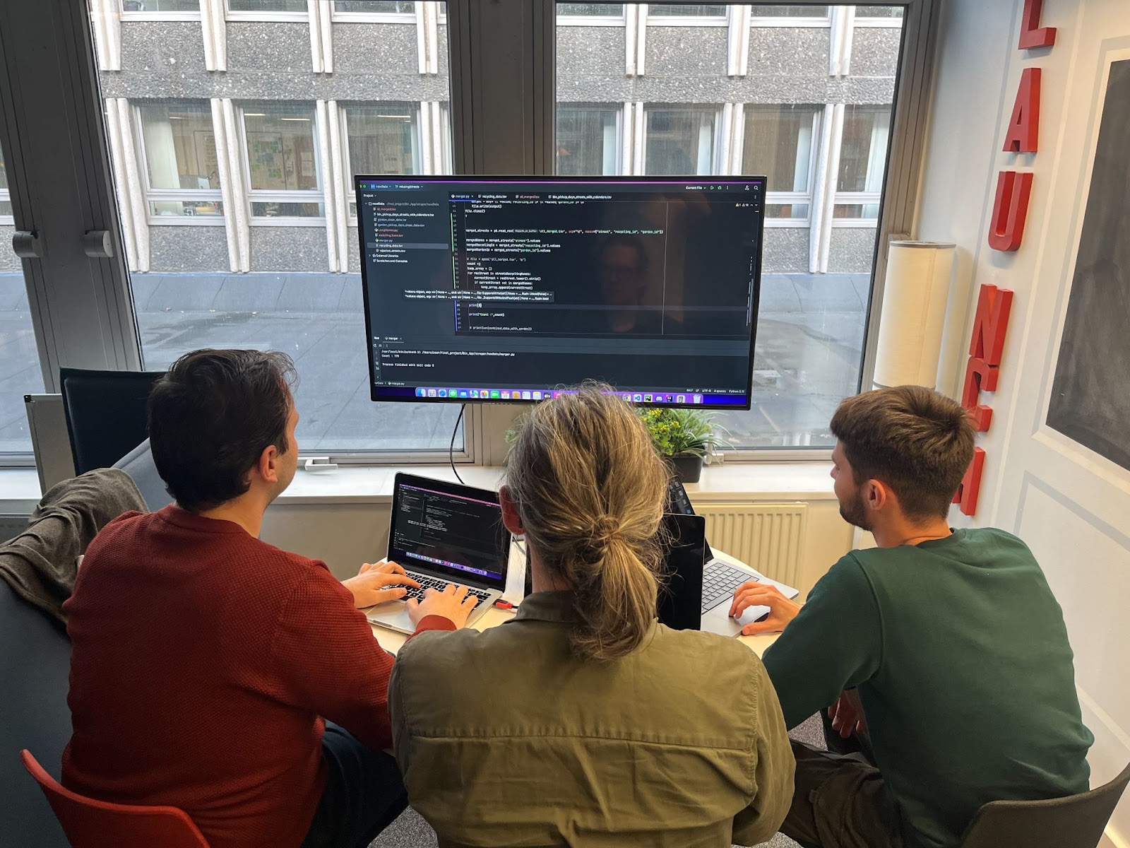 three students coding together around a big screen