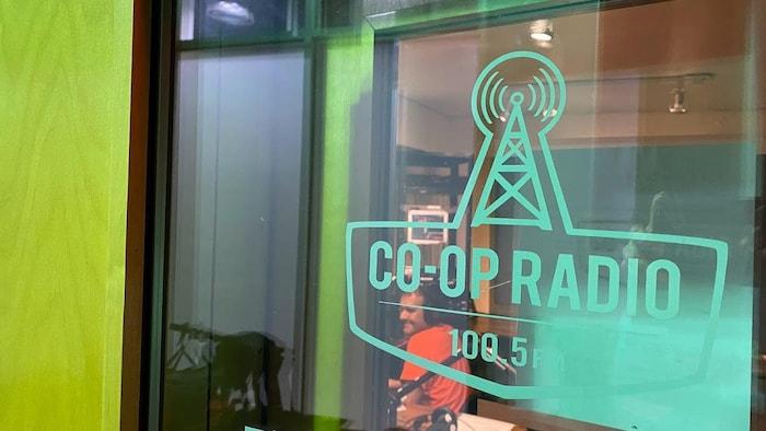 El logotipo de Coop Radio de Vancouver aparece en una ventana a través de la cual se ve el estudio de transmisión.  / Le logo de Coop Radio de Vancouver figure sur une fenêtre à travers laquelle on peut voir le studio de diffusion.