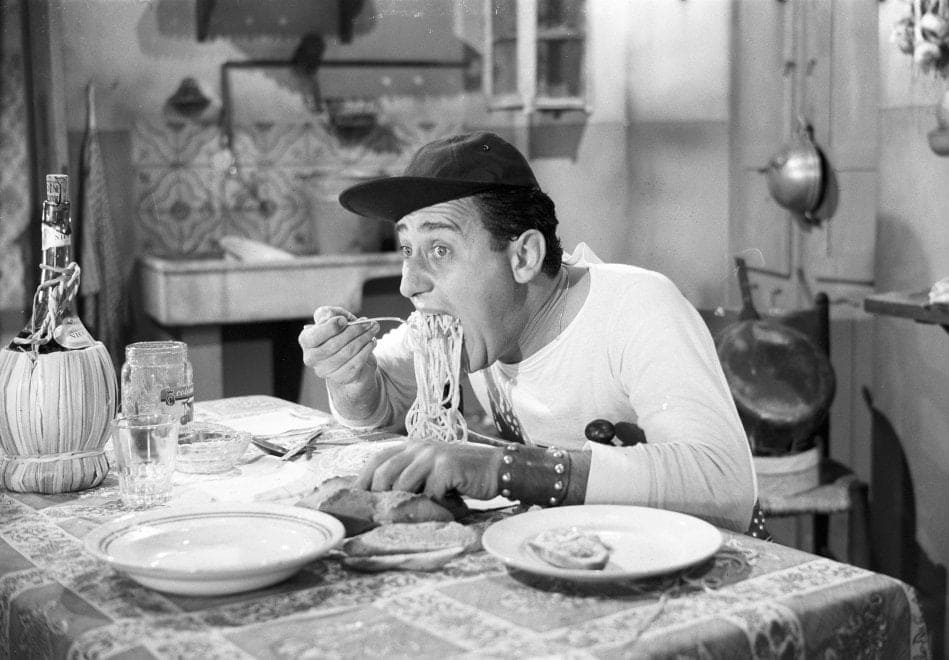 Scena iconica di Alberto Sordi, mentre mangia gli spaghetti nel film Un Americano A Roma, in bianco e nero. 