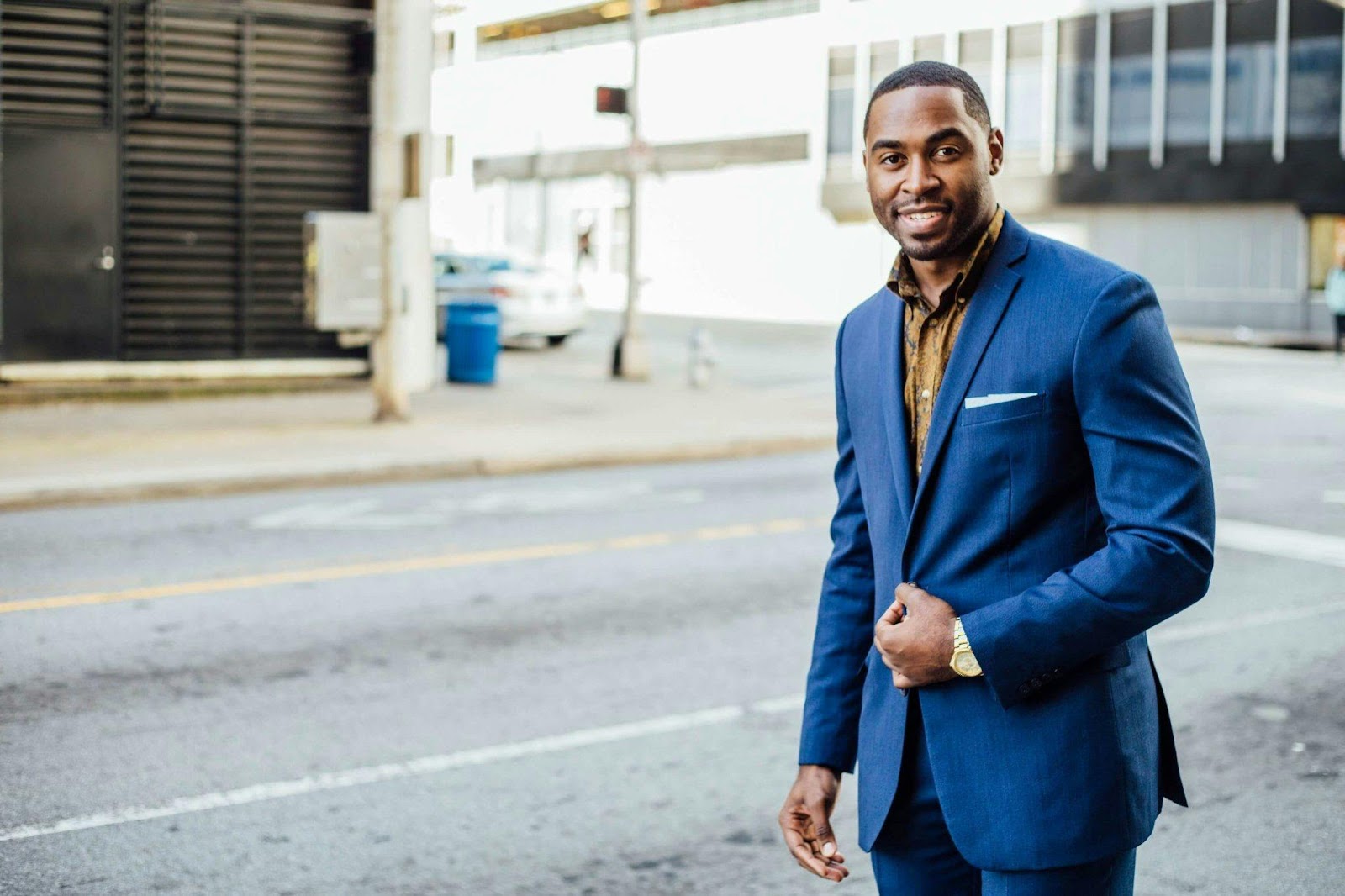 A young african american man standing on a city street with a blue businee blazer starting his job search and path to success.