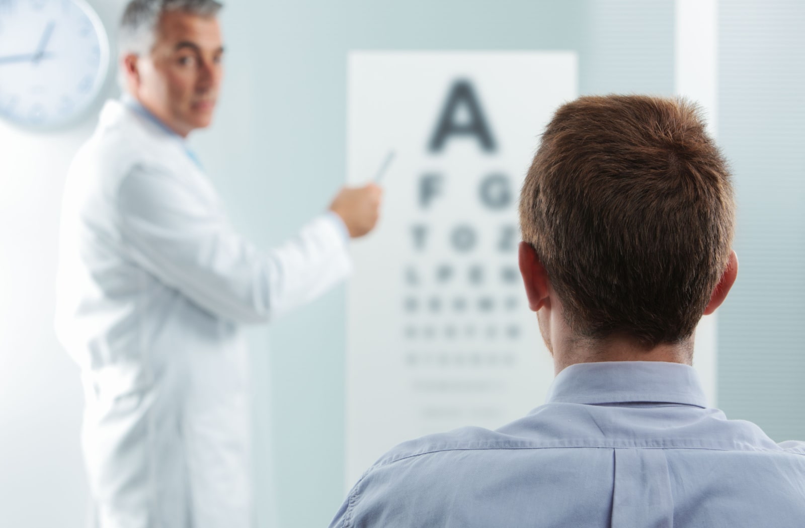 A male optometrist instructing a male patient to read letters off of a Snellen eye chart.