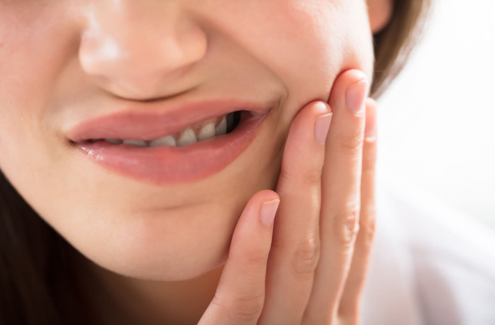 A close-up image of a woman touching her face while experiencing toothache discomfort.