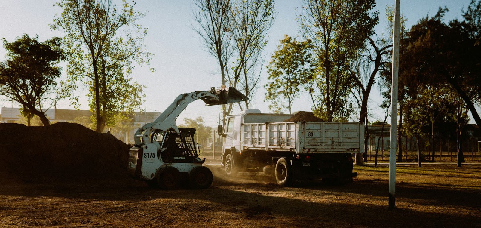 {A skid steer loader loading dirt into a dump truck, showcasing heavy construction equipment in action
