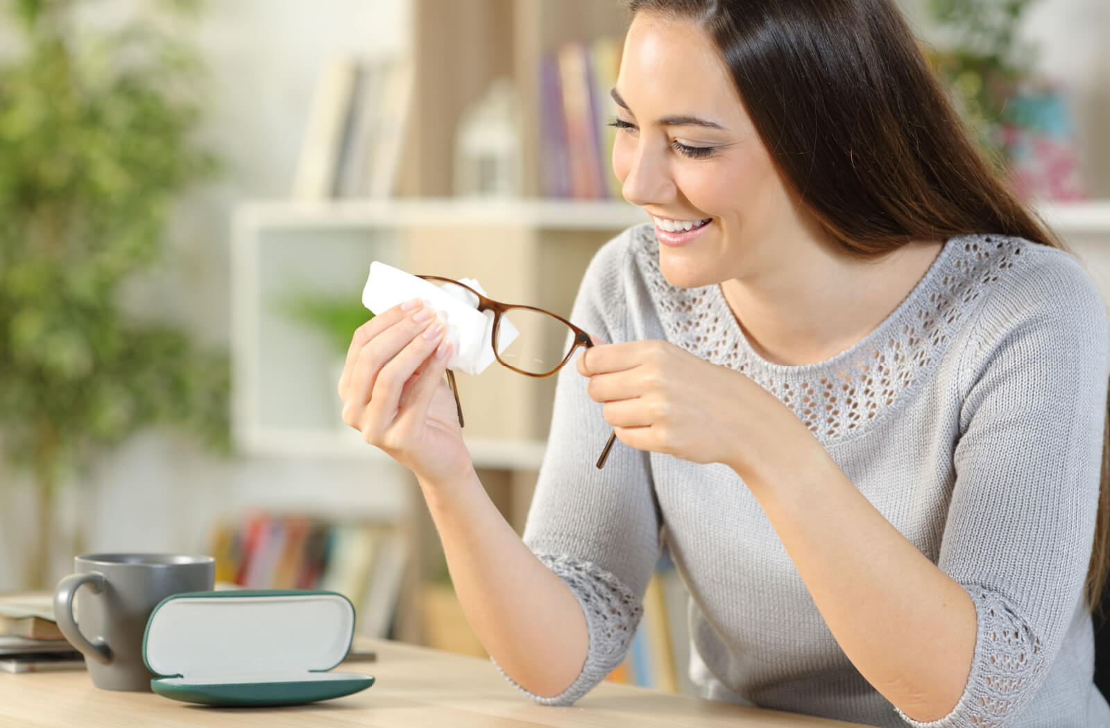 A young woman cleaning her eyeglasses with a white microfibre cloth.