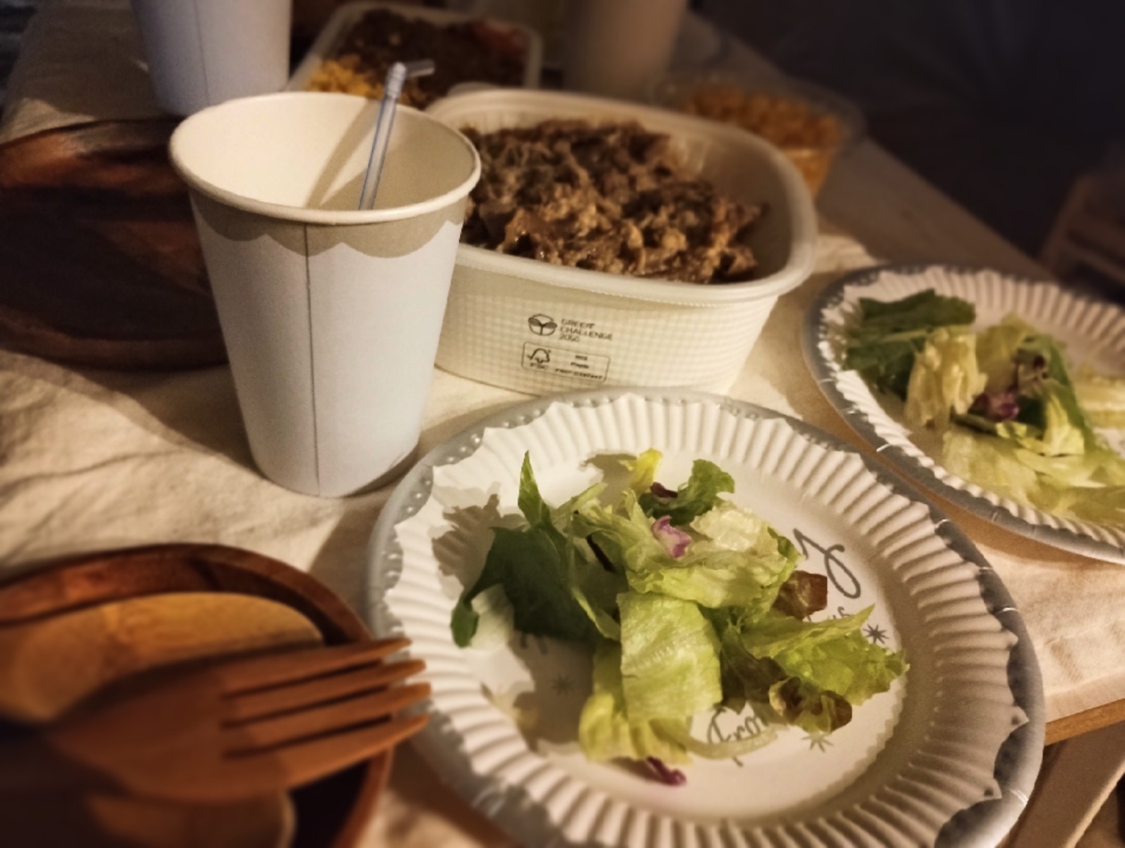 紙皿に載せられた野菜サラダや、髪の容器に入った食事、紙コップに入った飲み物が並んでいる。
