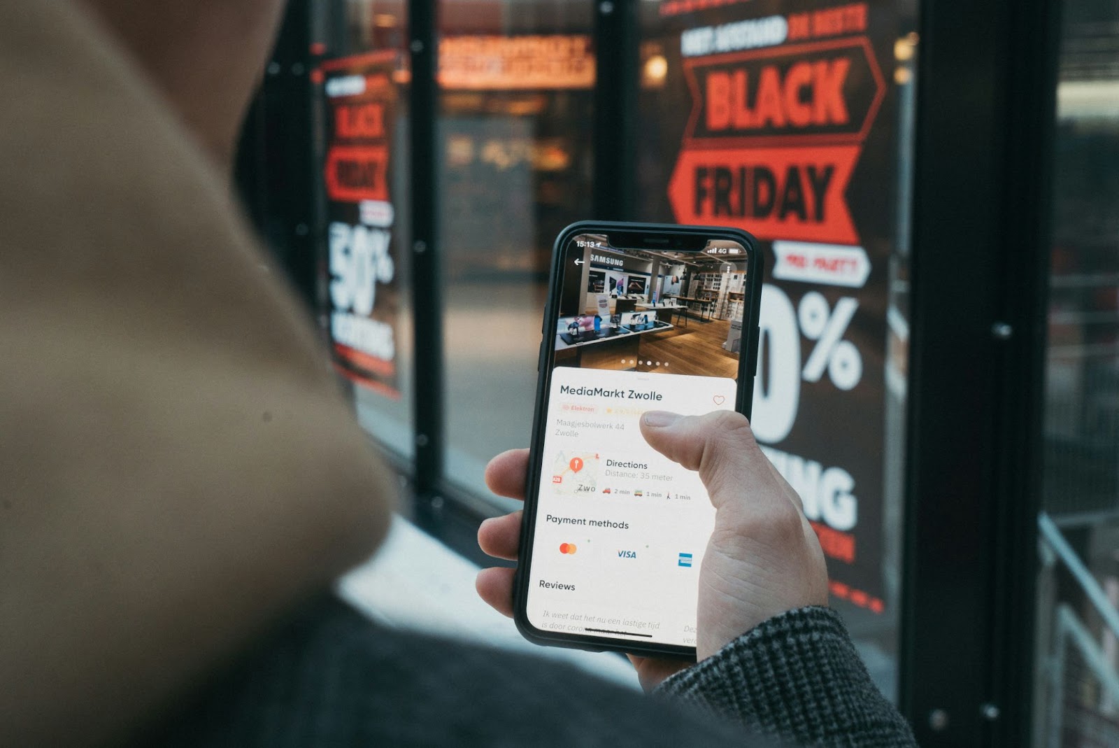 A person holding a cell phone in his hand, in the background, you can see an image of sales in a display case