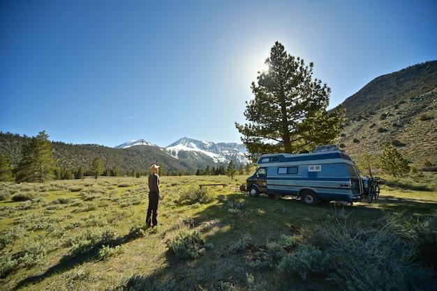 Beautiful shot of a female standing on a grassy field near a van with mountain