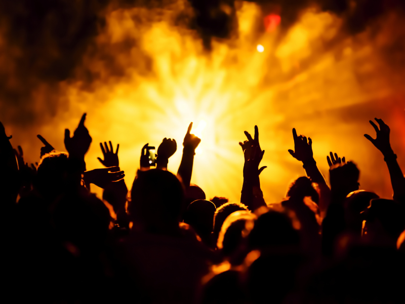 A crowd of people dancing at a music concert with pyrotechnics.