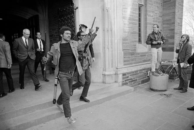 Toting a rifle and raising a clenched fist, Thomas W. Jones, spokesman for the Afro-American Society at Cornell University at Ithaca, N.Y., marches out of a student union hall after black militants occupied the building in a showdown over race relations, April 20, 1969. (AP Photo/Steve Starr)