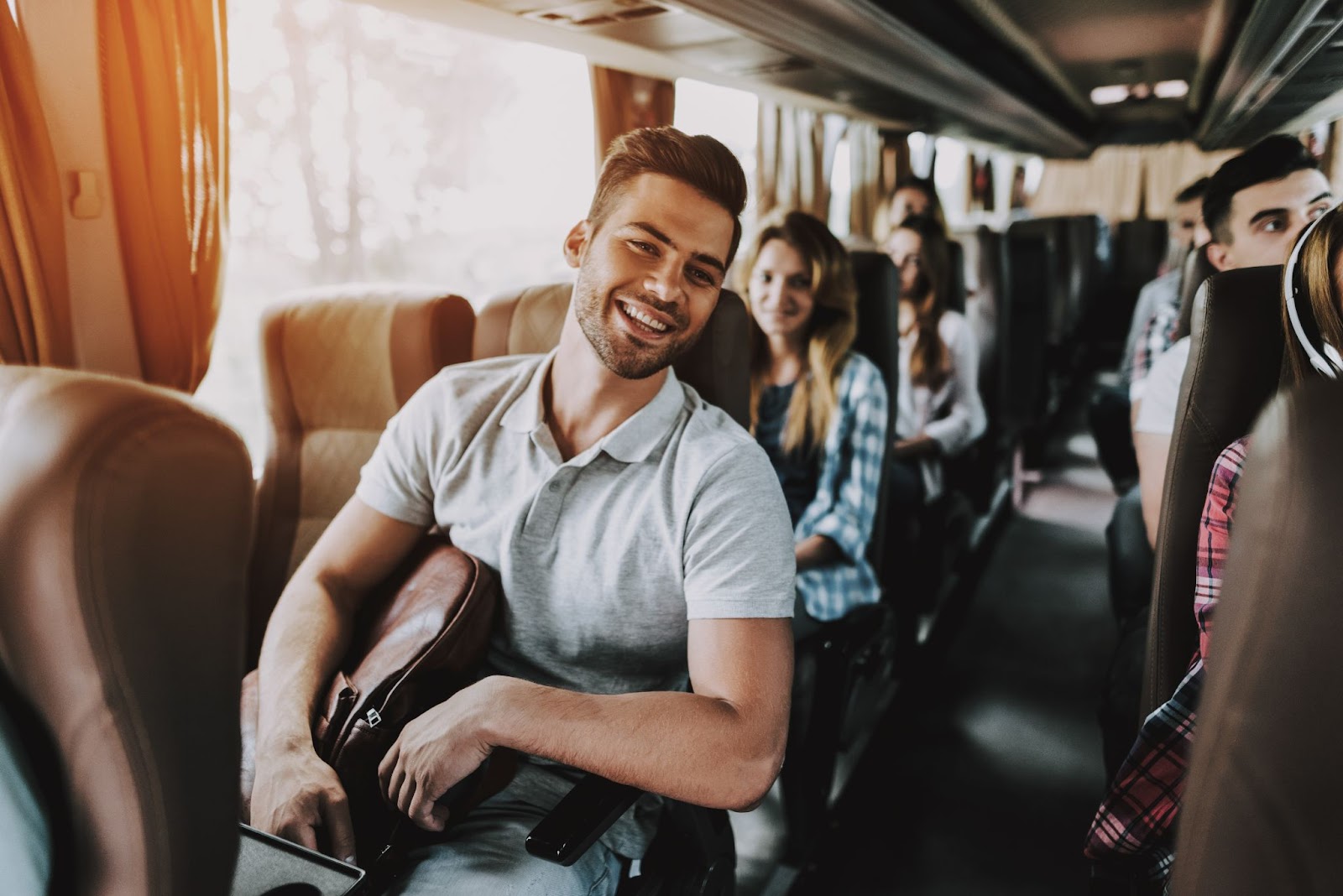 Homem sorrindo sentado dentro de um ônibus de viagem. Outros passageiros ocupam as poltronas do veículo.