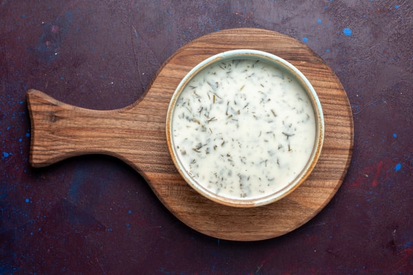 A bowl of alfredo sauce served on a wooden board