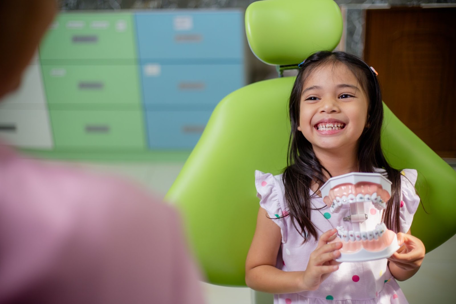 little asian girl sitting in the chair smiling at the dentist holding a teeth mould